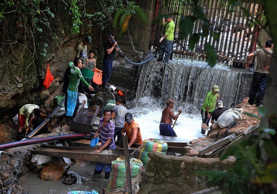 A group of people, including women and children, search for gold in fine sand in a river called Cianurada — “cyanide-filled river.” The gold-laced water comes from processing at the Gran Colombia Gold Corporation factory in the mining town of Segovia, Colombia.