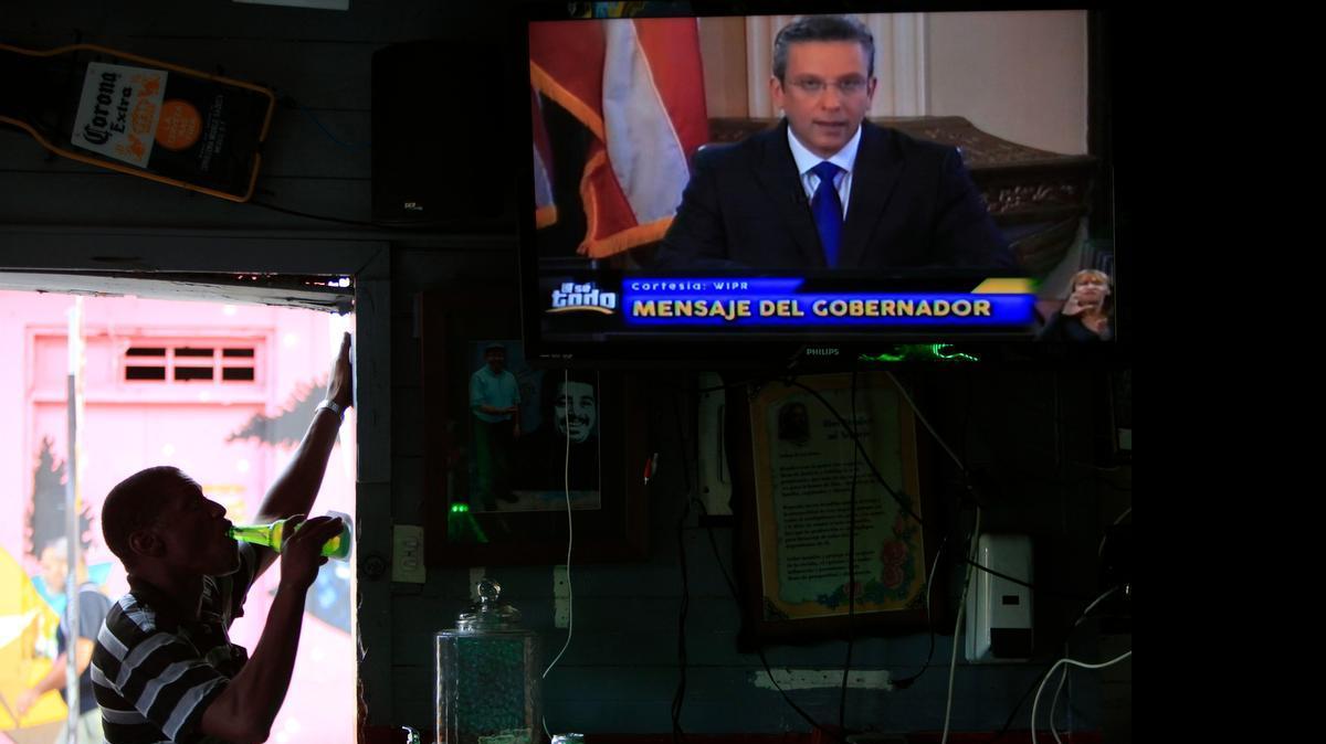 
A man drinks a beer in a local bar as he watches Puerto Ricos governor Alejandro Garcia Padilla on television delivering an address on the state of the island's finances, in San Juan, Puerto Rico, Monday, June 29, 2015. The governor said that he will form a financial team to negotiate with bondholders on delaying debt payments and then restructuring $72 billion in public debt that he says the island can't repay. 
