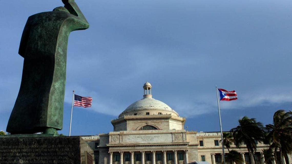 In this July 29, 2015, photo, a bronze statue of San Juan Bautista stands in front of Puerto Rico’s capitol flanked by U.S. and Puerto Rican flags, in San Juan. A federal control board on Friday, Sept. 30, 2016, took over Puerto Rico's finances and several government agencies for the first time in the U.S. territory's history in a bid to haul the island out of an acute economic crisis.