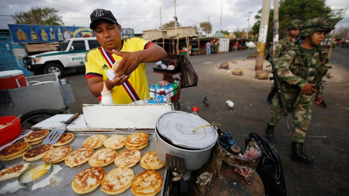 
A man sells arepas as Colombian soldiers patrol the border bewteen Colombia and Venezuela, in Paraguachon, Colombia, Wednesday, Sept. 9, 2015. Venezuelan President Nicolas Maduro has expanded an anti-smuggling offensive along the country's frontier with Colombia, and ordered another main crossing, this one in Paraguachon, closed Monday night as part of a two-week-old anti-smuggling offensive. 
