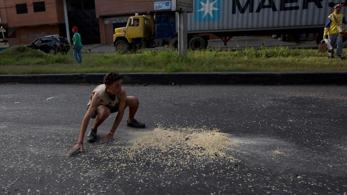 In this Jan. 23, 2018, photo, a youth moves quickly to collect grains of corn from the street that fell from a truck after it was looted outside the port in Puerto Cabello, Venezuela. At the country’s biggest port, people swarmed a corn-carrying truck and began filling up sacks with the grain while the driver was held at gunpoint.