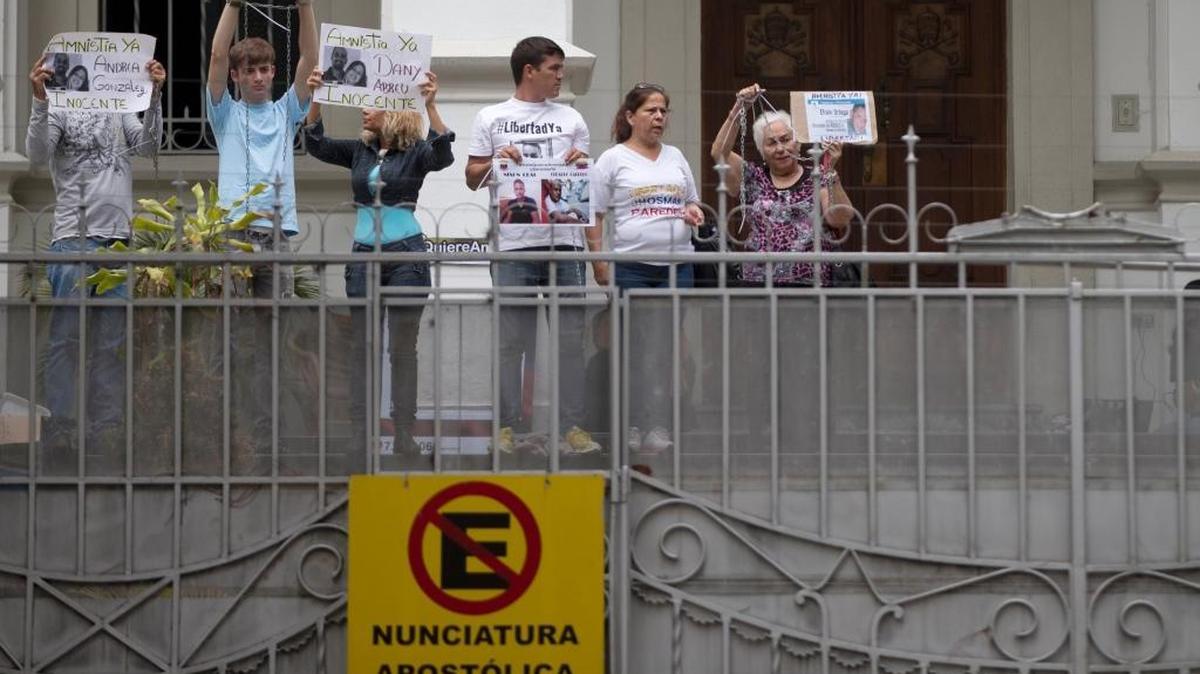 Protesters who say they have family members who are political prisoners hold up chains and signs showing their jailed relatives' faces at the Apostolic Nunciature building in Caracas, Venezuela, Tuesday, April 5, 2016. Dozens protested to ask Pope Francis to mediate with the government in favor of an amnesty law that would free the prisoners, which was passed last week by the opposition majority in the National Assembly. President Nicolas Maduro is expected to veto the measure.