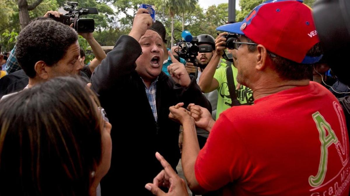 Opposition lawmaker Jose Dionisio Brito, left, holds up a copy of Venezuela's Constitution as he argues with a supporters of Venezuela's President Nicolas Maduro during a protest outside of Venezuela's General Prosecutor's office in Caracas, Venezuela, Friday, March 31, 2017. Venezuelans have been thrust into a new round of political turbulence after the government-stacked Supreme Court gutted congress of its last vestiges of power, drawing widespread condemnation from foreign governments and sparking protests in the capital.