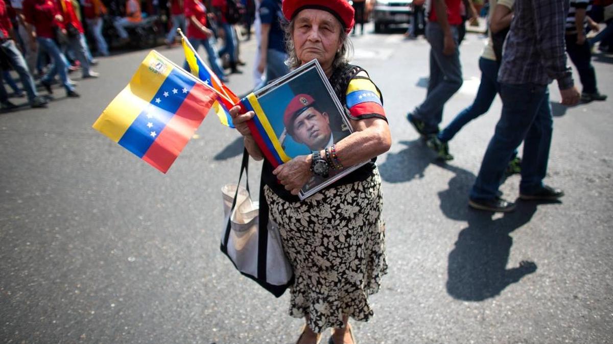 In this Thursday, Feb. 4, 2016 photo, Marina Parra holds a picture of Venezuela's late President Hugo Chavez and wears a replica of his signature red beret during a parade marking the anniversary of his failed coup, in Caracas, Venezuela. Chavez, a former paratrooper, led a failed coup in 1992 before being democratically elected president six years later. Chavez died of cancer in March 2013 at the age of 58.