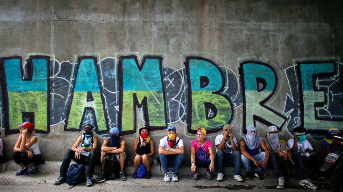 Anti-government demonstrators sit under a bridge that has graffiti written in Spanish that reads "Hunger," during a protest in Caracas, Venezuela, Saturday, July 1, 2017. Demonstrators are taking to the streets after three months of continued protests that has left dozens dead and seen the country's chief prosecutor Luisa Ortega barred from leaving the country and her bank accounts frozen following her mounting criticisms of President Nicolas Maduro.