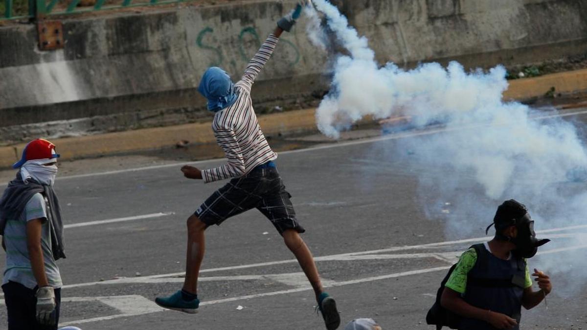 A demonstrator returns a tear gas canister to National Guard soldiers, during clashes with security forces on the Francisco Fajardo highway, outside La Carlota Air Base in Caracas, Venezuela, Friday, June 23, 2017. More than 70 people have been killed during almost 90 days of protests seeking President Nicolas Maduro's removal.