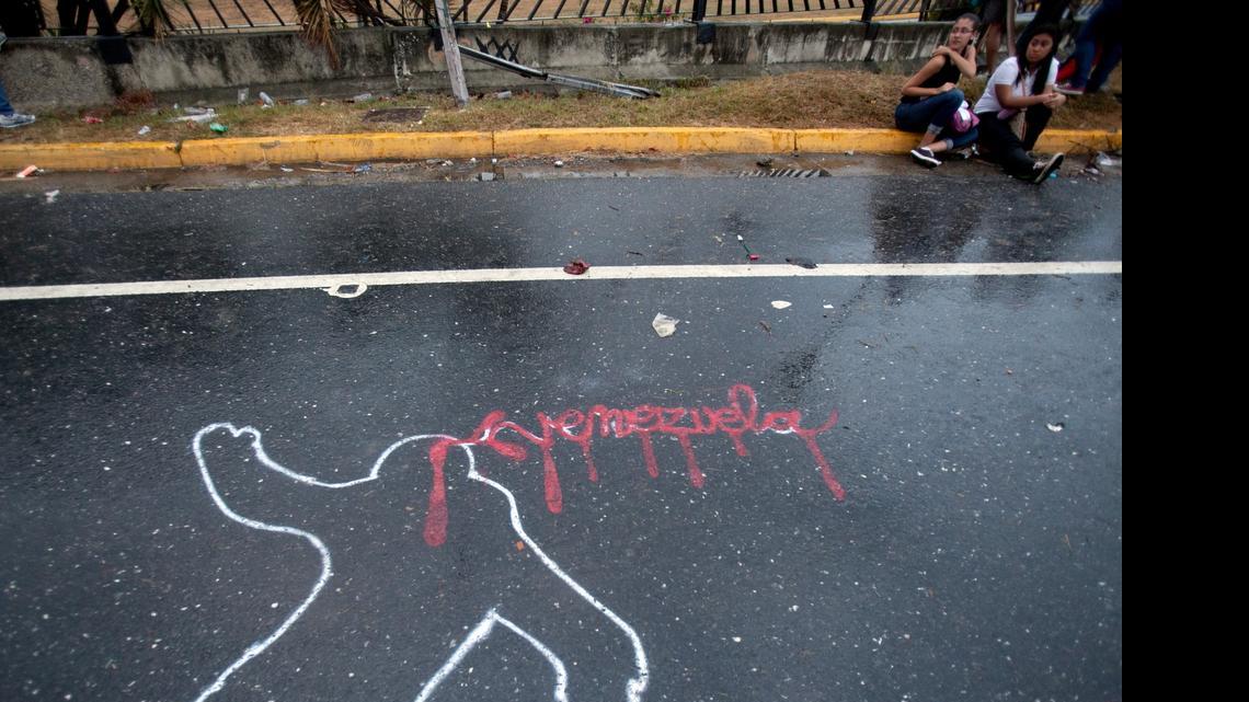 
In this Feb. 18, 2014 file photo, demonstrators rest from taking part in an opposition protest next to the outline of a body, representing a police chalk outline, with Venezuela written in red, to symbolize blood, in Caracas, Venezuela. 
