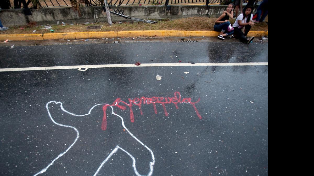
In this Feb. 18, 2014 file photo, demonstrators rest from taking part in an opposition protest next to the outline of a body, representing a police chalk outline, with Venezuela written in red, to symbolize blood, in Caracas, Venezuela. 
