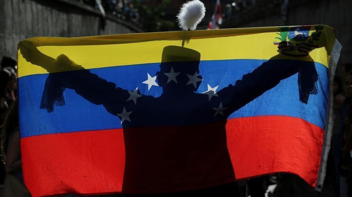 A demonstrator dressed as Venezuelan independence hero Simón Bolivar is silhouetted against a national flag during a tribute to the dead on July 24 in Venezuela.