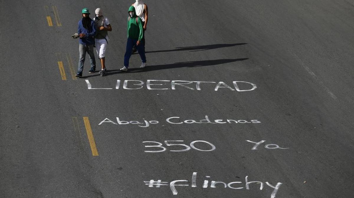 Anti-government demonstrators walk past a message written on the road that reads in Spanish: "Freedom. Down with the chains. 350 now." during protests calling for elections in Caracas, Venezuela, Wednesday, June 14, 2017. The number 350 is a reference to Venezuela's constitution which gives to the right to rebel against injustice.