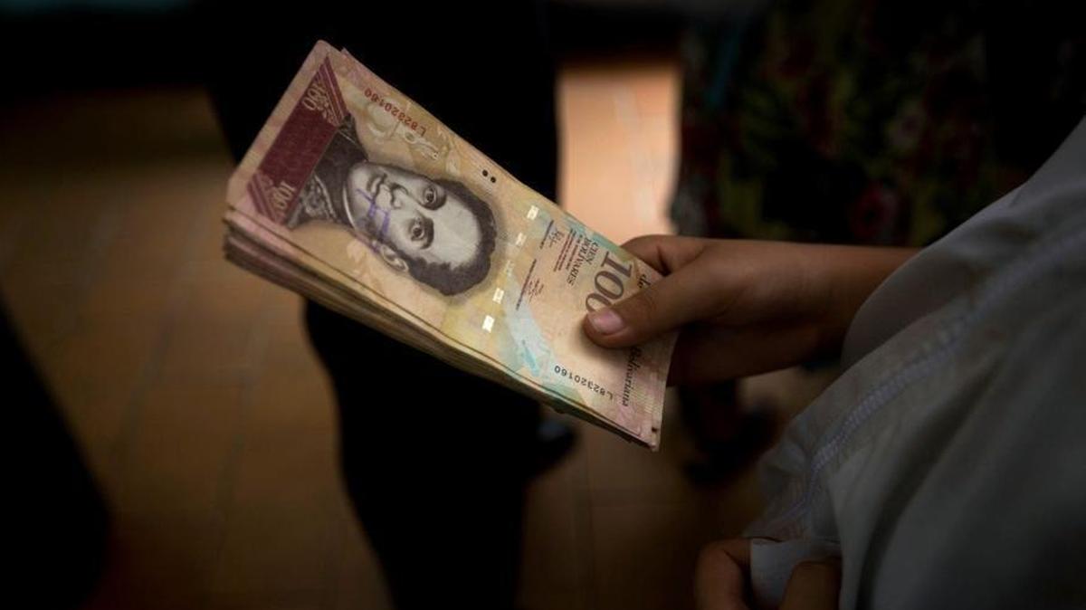 A customer holds a stack of 100 bolívar notes at a bakery in downtown Caracas, Venezuela.