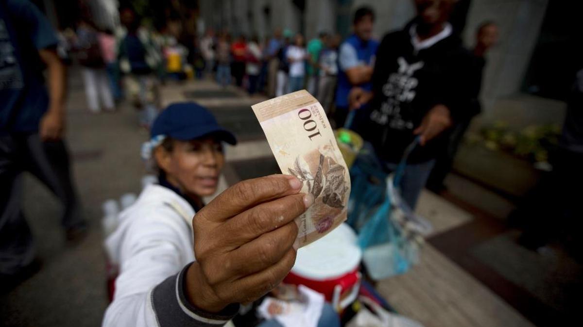 A street vendor inspects the authenticity of a 100 bolivar note as people stand in line outside a bank to deposit their 100 bolivar bank notes in Caracas, Venezuela, on Tuesday, Dec. 13, 2016.