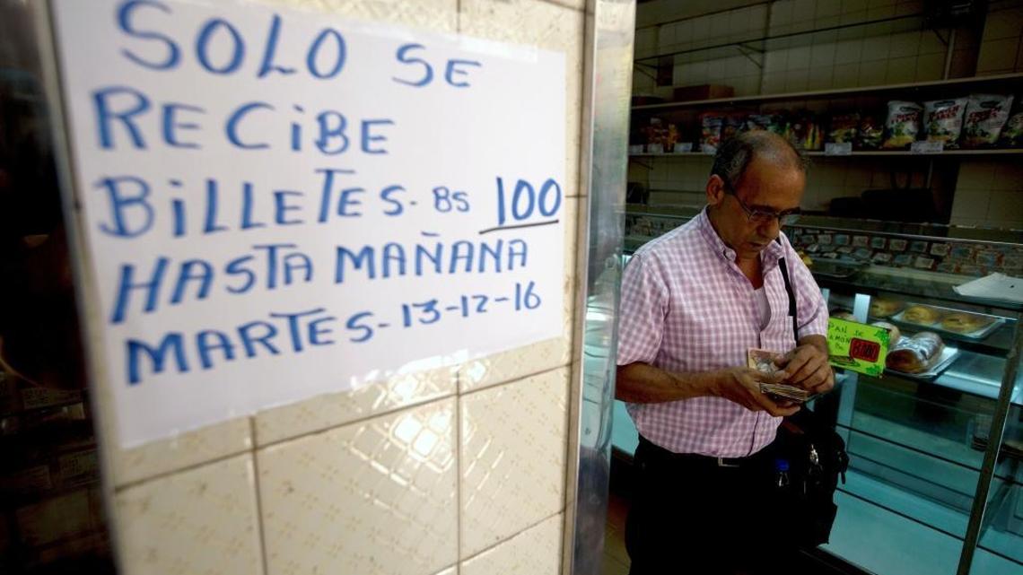 A man counts his 100-bolivar notes next to a sign alerting customers with a message in Spanish that reads: “100-bolivar notes will only be received until Tuesday, 12-13-16,” inside a bakery in downtown Caracas on Monday. Venezuelans are rushing to spend their 100-bolivar notes after a surprise announcement that they will be taken out of circulation this week.