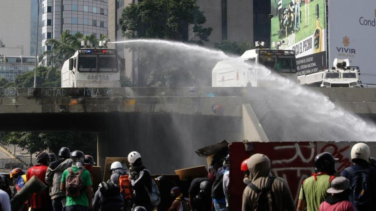 Protesters take cover from the riot police water cannon during a march in Caracas, Venezuela, Monday, May 29, 2017.