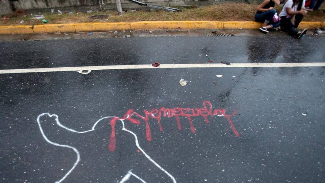 Demonstrators rest from taking part in a 2014 opposition protest in Caracas next to the outline of a body, representing a police chalk outline, with Venezuela written in red to symbolize blood.