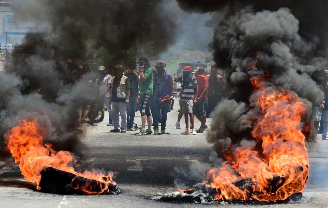 Anti-government activists stand near a roadblock burning in flames in Valencia.