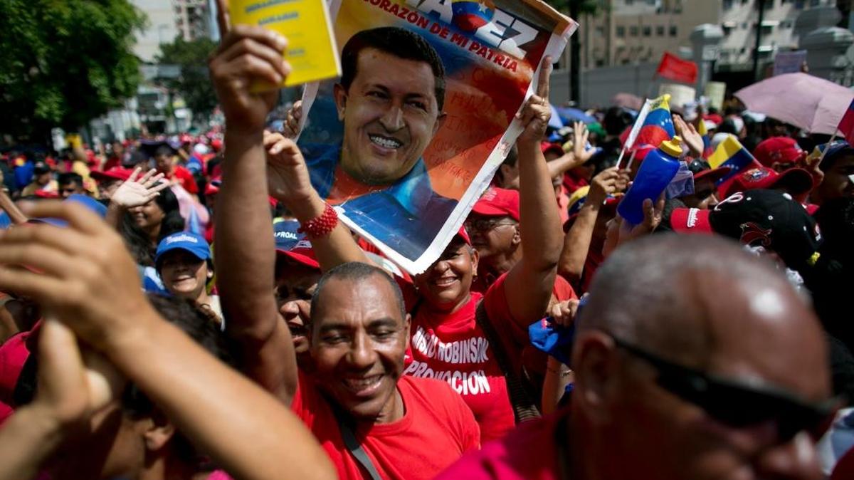 In this Oct. 28, 2016, photo, a government supporter holds up a poster of Venezuela's late President Hugo Chavez during a rally in support of President Nicolas Maduro, outside Miraflores presidential palace in Caracas, Venezuela.