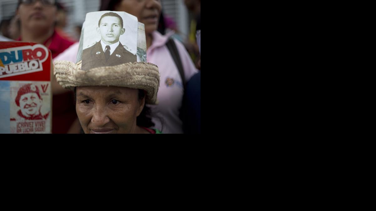 
A woman wears a hat decorated with a picture of Venezuela's late President Hugo Chavez, when he was a soldier, outside the 4F military museum where he's buried during a gathering to mark the second year anniversary of his death in Caracas, Venezuela, Thursday, March 5, 2015. Chavez died at age 58 on March 5, 2013. 
