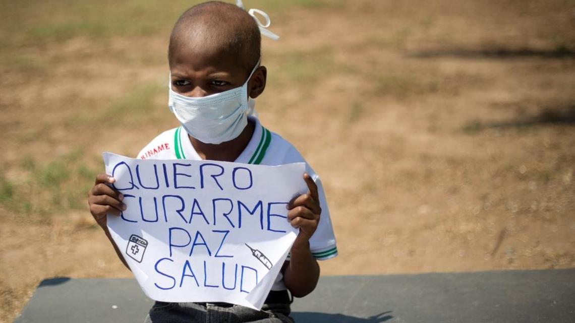 In this Feb. 26, 2016 file photo, Oliver Sanchez, diagnosed with non-Hodgkin's lymphoma, holds a sign with a message that reads in Spanish; "I want to be cured, peace, health" during a protest against the growing shortage of medicines and medical supplies, in Caracas, Venezuela. The eight-year-old boy who had become a symbol of Venezuela's medical crisis, died.