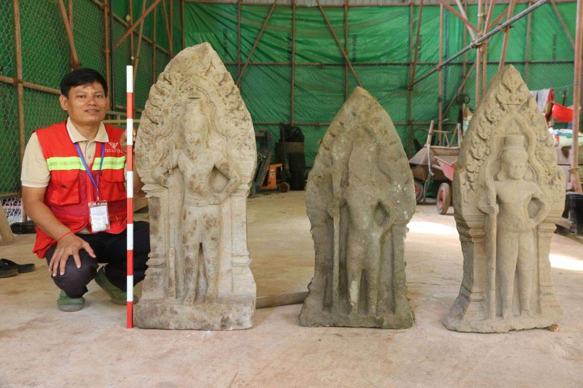 An archaeologist kneels next to three 900-year-old guardian statues.