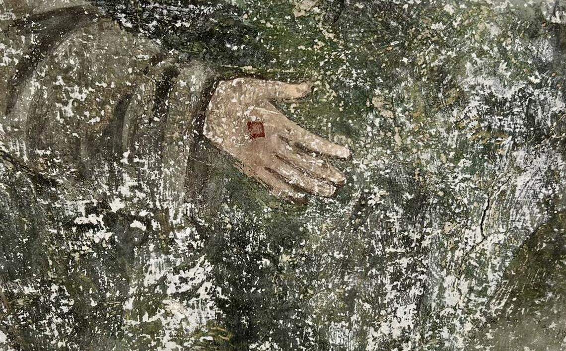 A painting showing the hand of a friar dressed in green garb.
