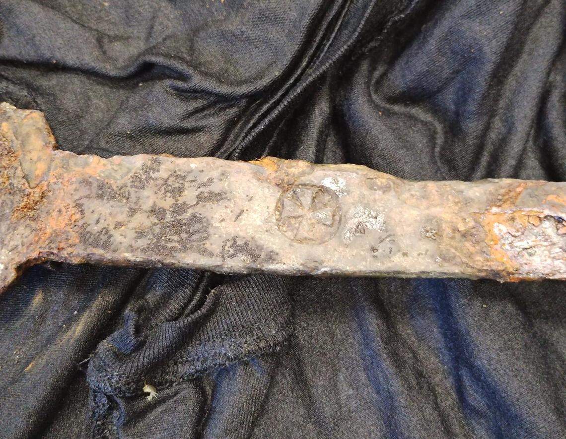 A close-up photo shows a cross-like design on the handle of the medieval sword.