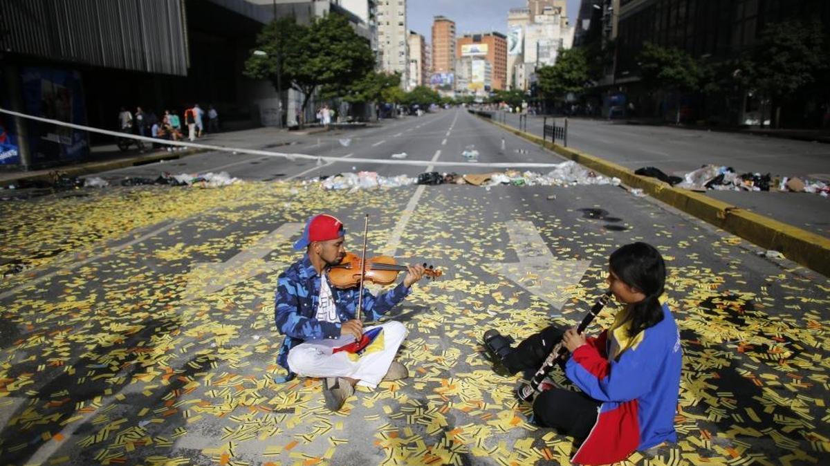 Musicians play their instruments as they sit in the middle of a road littered with metro tickets at a roadblock set up by anti-government protesters in Caracas on Thursday.