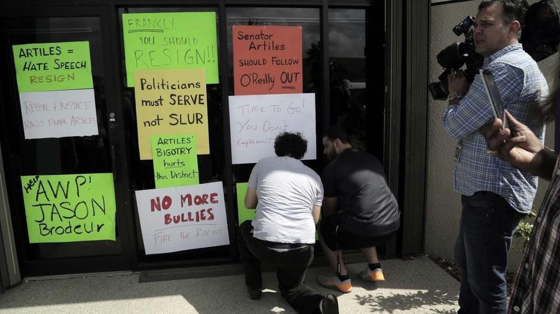 Protesters tape signs on the entrance to the office of state Sen. Frank Artiles’ Miami district office.