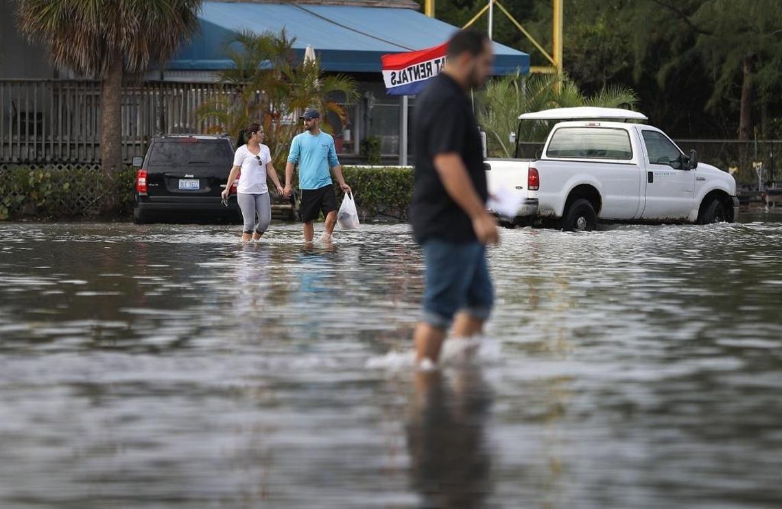 Yaneisy Duenas (L) and Ferando Sanudo walk through the flooded parking lot to their boat at the Haulover Marine Center on November 14, 2016 in North Miami, Florida. The flood waters are caused by the combination of the lunar orbit which causes seasonal high tides, also known as a King tide, and what some scientists believe is rising sea levels due to climate change.