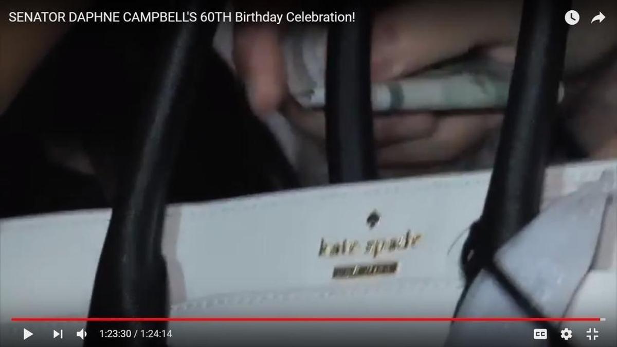 Video posted on Sen. Daphne Campbell’s YouTube page shows a campaign donor giving her a Kate Spade purse and then placing several hundred dollars inside. Campbell says the money was a joke.