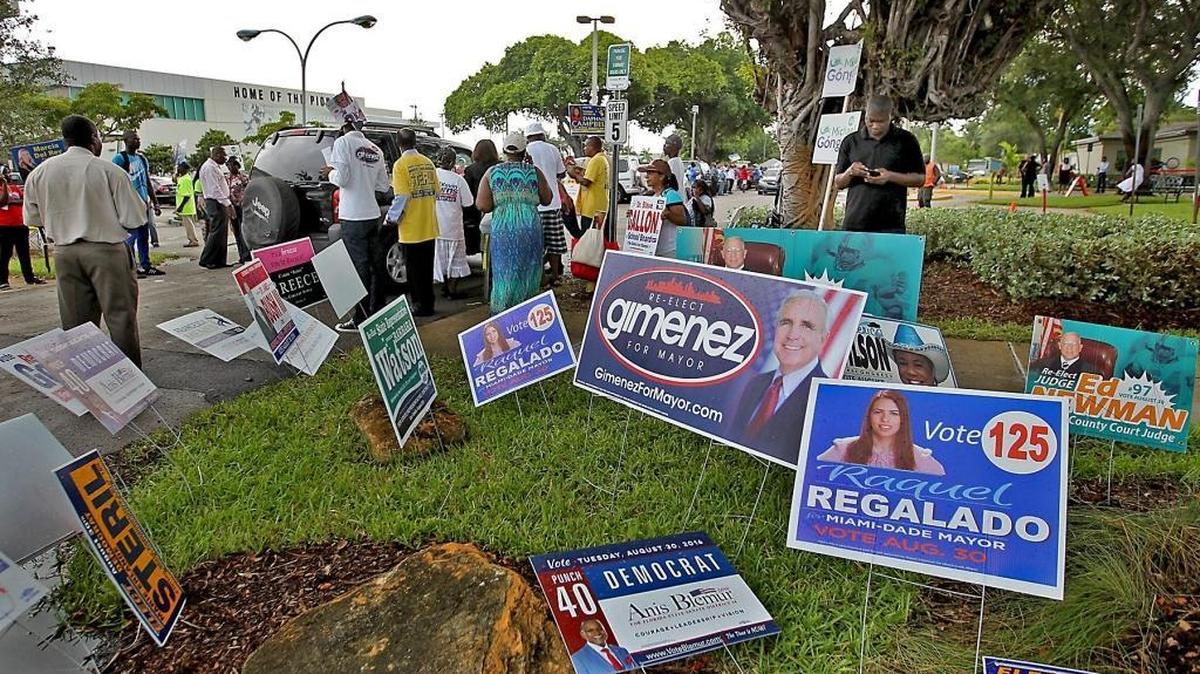 Campaign workers approach voters as they go to cast their votes during a ‘Souls to the Polls’ event at the North Miami Library polling station on Sunday, August 28, 2016.