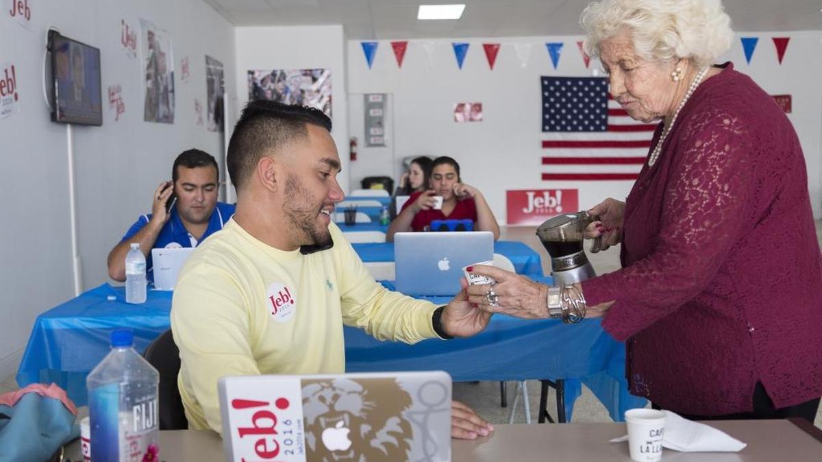 Silvia Caminero, 79, right, hands Medardo Cruz, 23, Cuban coffee while he dials voters in Iowa encouraging them to vote for Jeb Bush. Medardo and Caminero are both volunteers who came out to help Bush’s Miami field office on Jan. 9, 2016.
