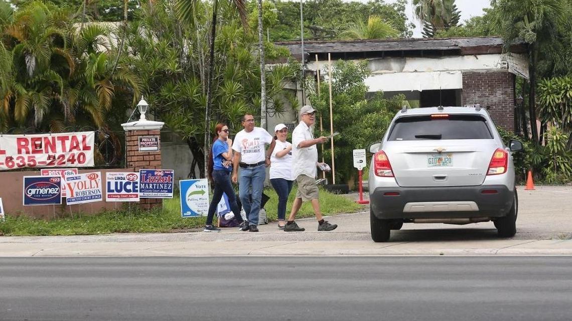 Campaign workers approach a voter in his car with candidate literature at the Polish-American Club of Miami.