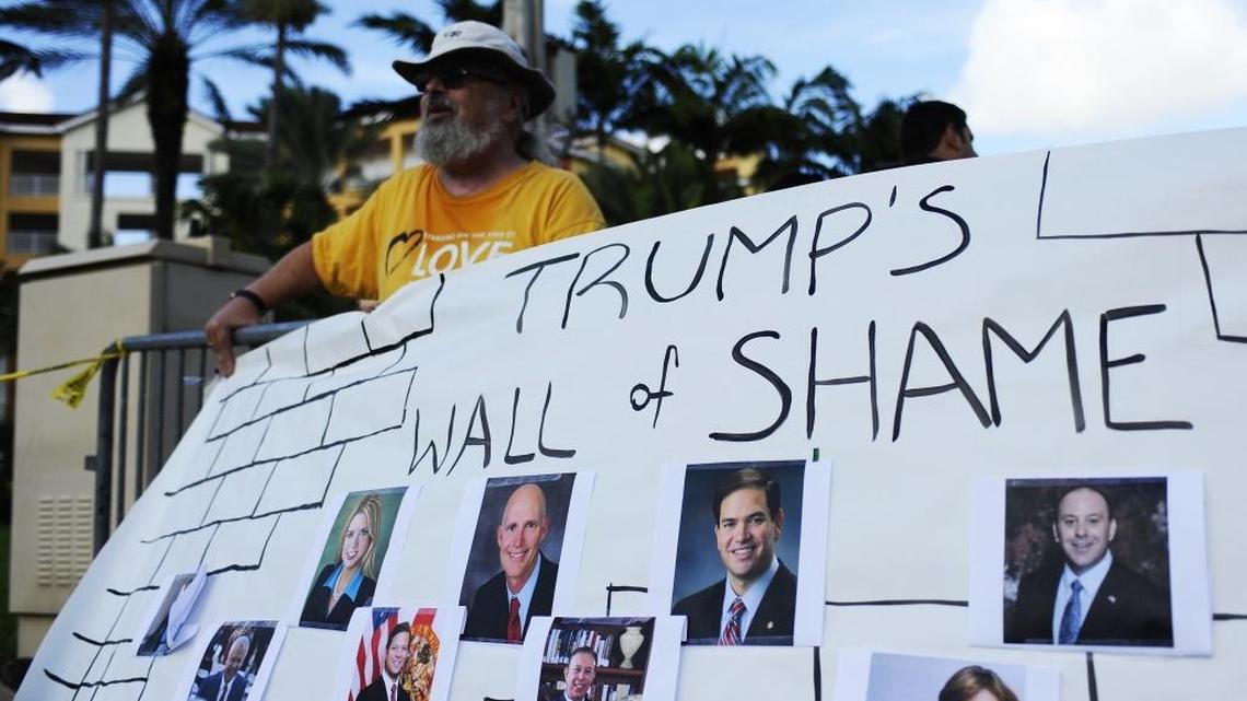 Bud Conlin stands behind a fence while holding a sign declaring, “Trump's Wall of Shame." He was protesting across the street from Trump National Doral Resort on Tuesday, July 26, 2016. Republican presidential nominee Donald Trump was holding a fundraiser at the resort.