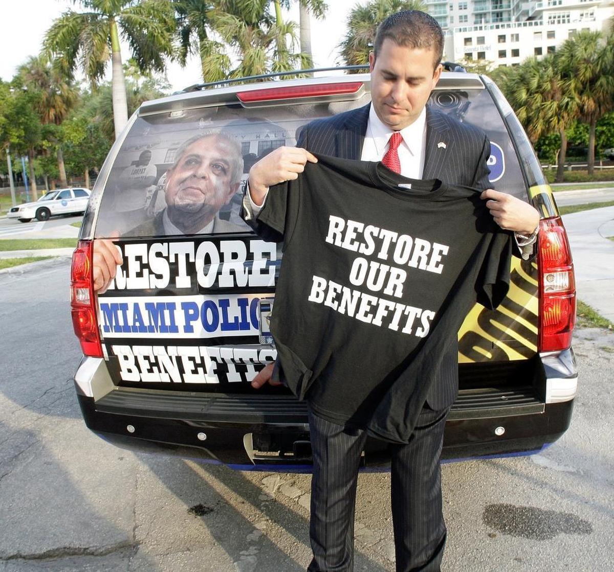 Miami Fraternal Order of Police President Javier Ortiz shows a “Restore Our Benefits” T-shirt before marching to Miami City Hall on March 27, 2014, to protest.