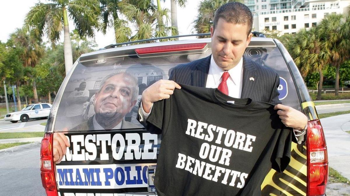 Miami Fraternal Order of Police President Javier Ortiz shows a “Restore Our Benefits” T-shirt before marching to Miami City Hall on March 27, 2014, to protest.