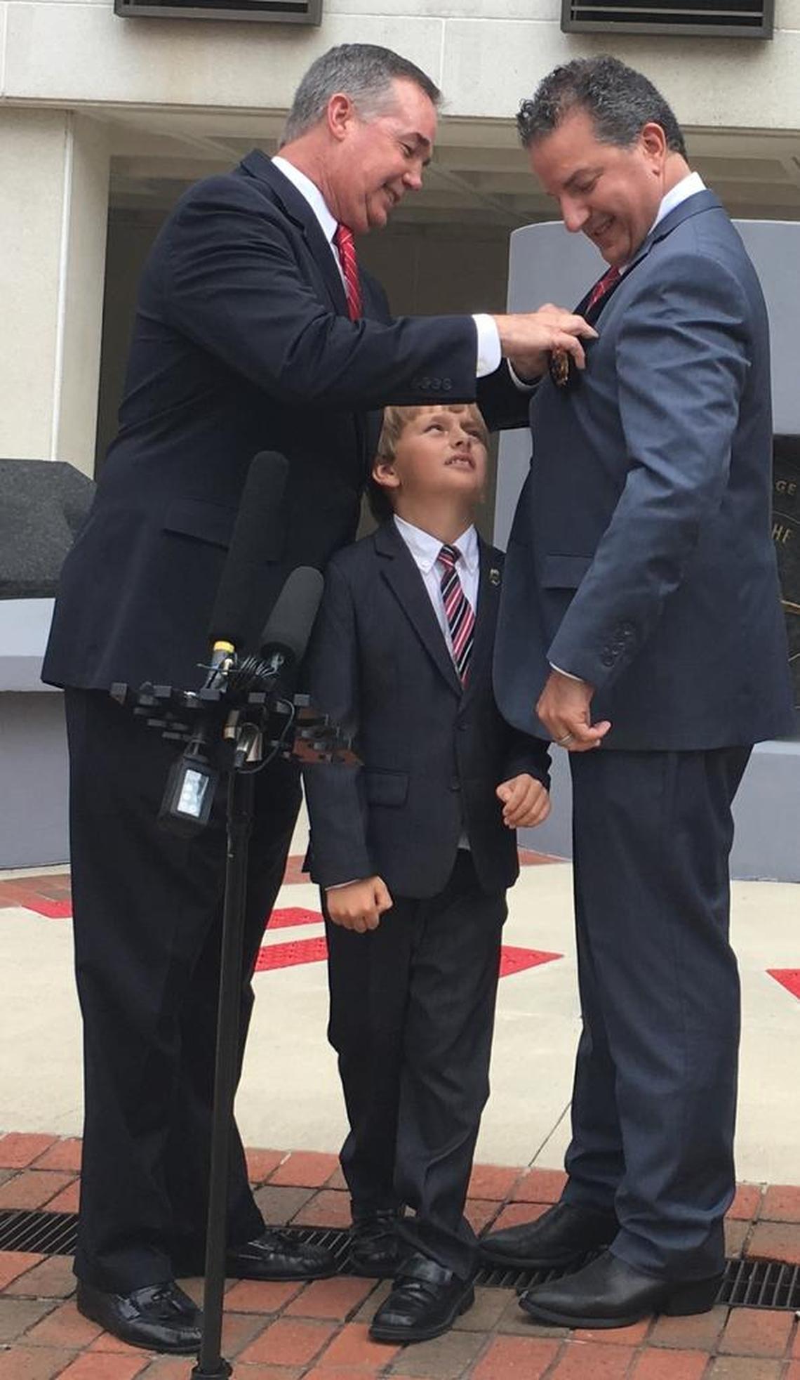 Outgoing Chief Financial Officer Jeff Atwater pins the state fire marshal badge on his successor, Jimmy Patronis, as Patronis’ son, Theo, looks up.