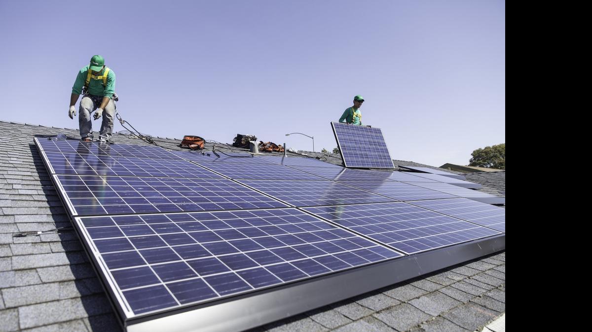 
Workers install solar panels on the roof of a home. 
