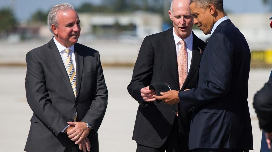 When President Obama came to Miami for an immigration town hall at Florida International University in February 2015, Gov. Rick Scott greeted him with a gift: a Miami Marlins baseball cap. Miami-Dade County Mayor Carlos Gimenez looks on.