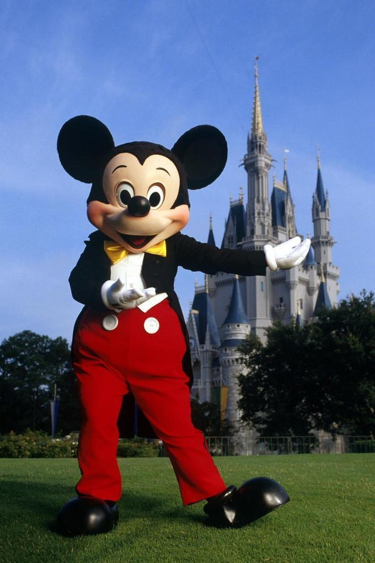 Standing in front of Cinderella Castle, Mickey Mouse greets guests at the Magic Kingdom.