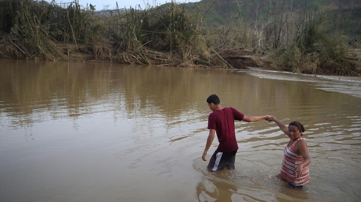 Hector Ojeda and Sonia Robles cross a river on foot after the bridge was washed away when Hurricane Maria passed through in Morovis, Puerto Rico. )