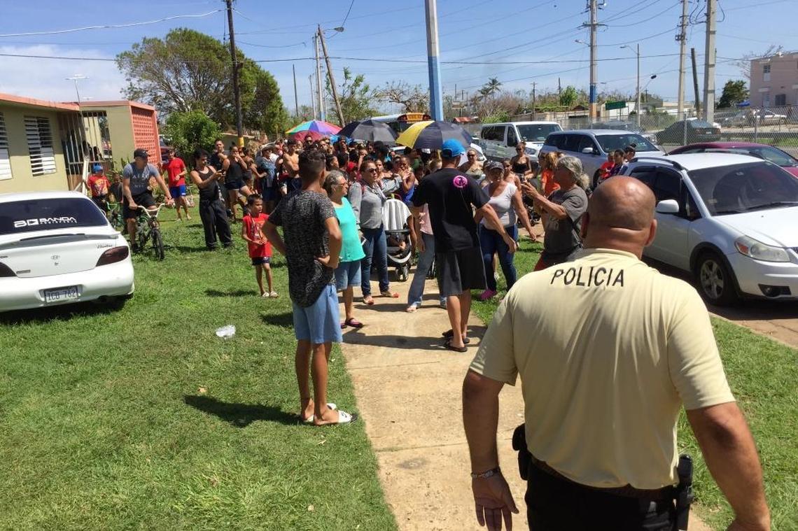 A police officer keeps an eye on a rapidly growing crowd in Aguadilla, Puerto Rico, Sunday Oct. 8, 2017, as soldiers arrive to offer rations of food and water.