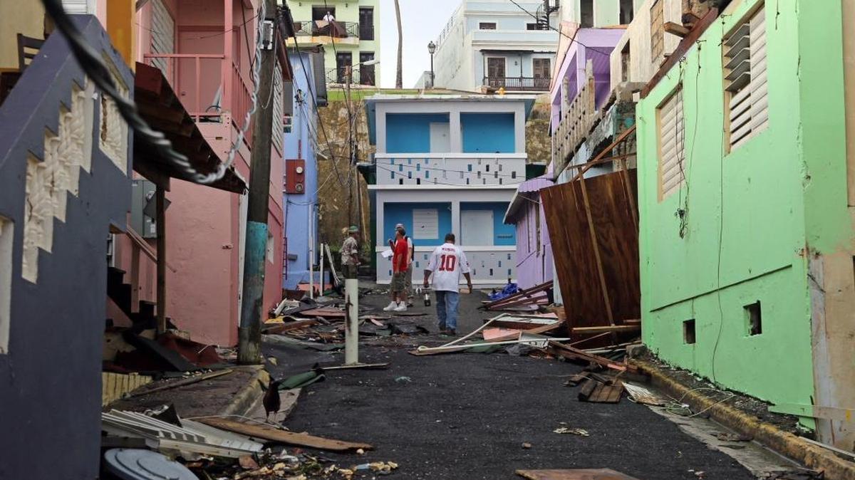 Man walks up near colorful damaged buildings. Residents of San Juan’s “La Perla” neighborhood have taken hurricane recovery into their own hands as they start the hard task of clean-up because of fear of being forgotten by the government. Hurricane Maria has left many of San Juan’s streets flooded and blocked by fallen power lines, trees, and debris as Puerto Rico tries to recover from the Category 4 storm on Thursday, Sept. 21, 2017.