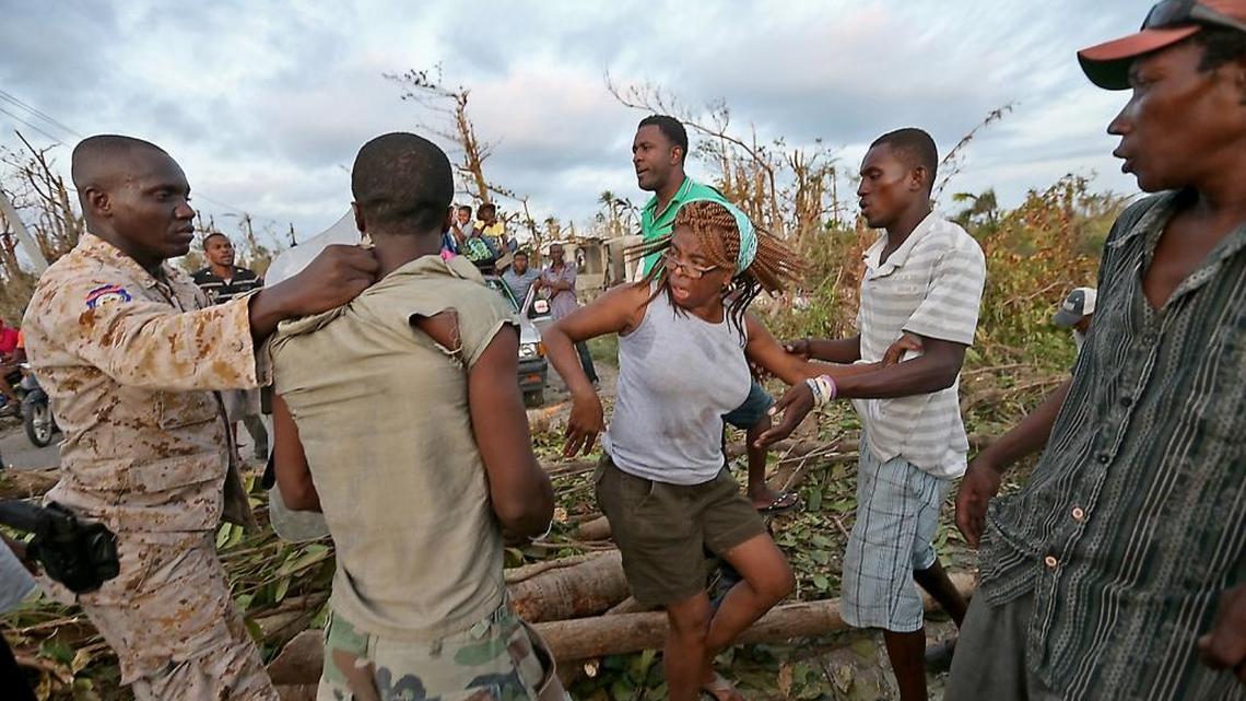 Fritza Charles is pushed out of the way as a Haitian National Police officer takes a man away from a protest where branches were spread across the middle of the road in Hock, Haiti, to block a convoy of food Saturday, Oct. 18, 2016.