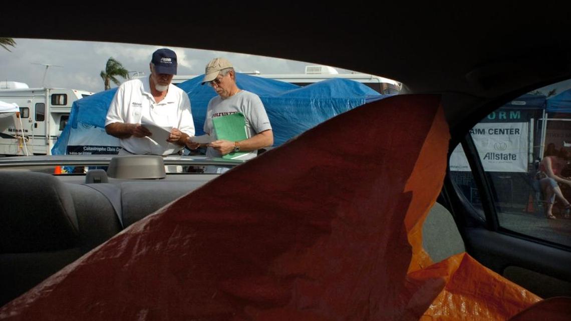 After Hurricane Wilma hit South Florida in 2005, Allstate insurance adjuster (left) Robert Cartier, talks to Frank Miller of Hollywood, about his Nissan Maxima. A shed fell on the rear of his car knocking out the window and scratching the car. The photo shows a tarp peeled back to keep the rain from further damaging the car.