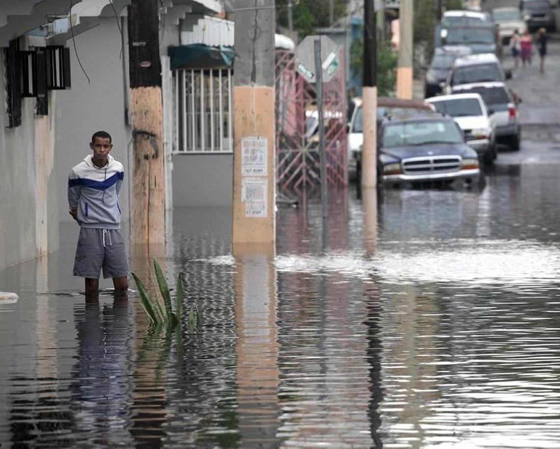 A man waits in knee-high water for a neighbor to open a door as residents throughout San Juan deal with Hurricane Maria’s aftermath leaving on Thursday.