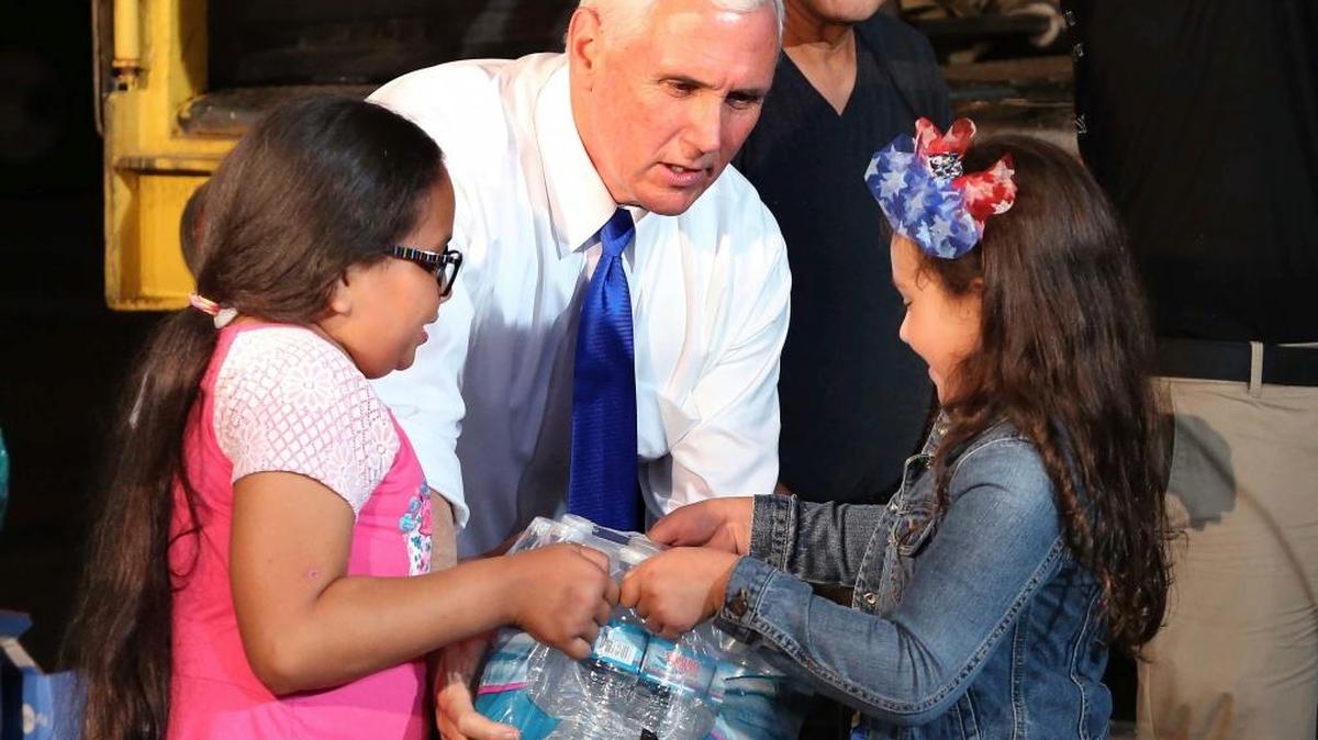 Emma Perez, 9, left, and Summer Muñoz, 7, hand Vice President Mike Pence a case of bottled water Thursday as he helps load a container bound for Puerto Rico, while visiting volunteers working on the relief effort for victims of Hurricane Maria at the Iglesia de Dios church in Kissimmee.