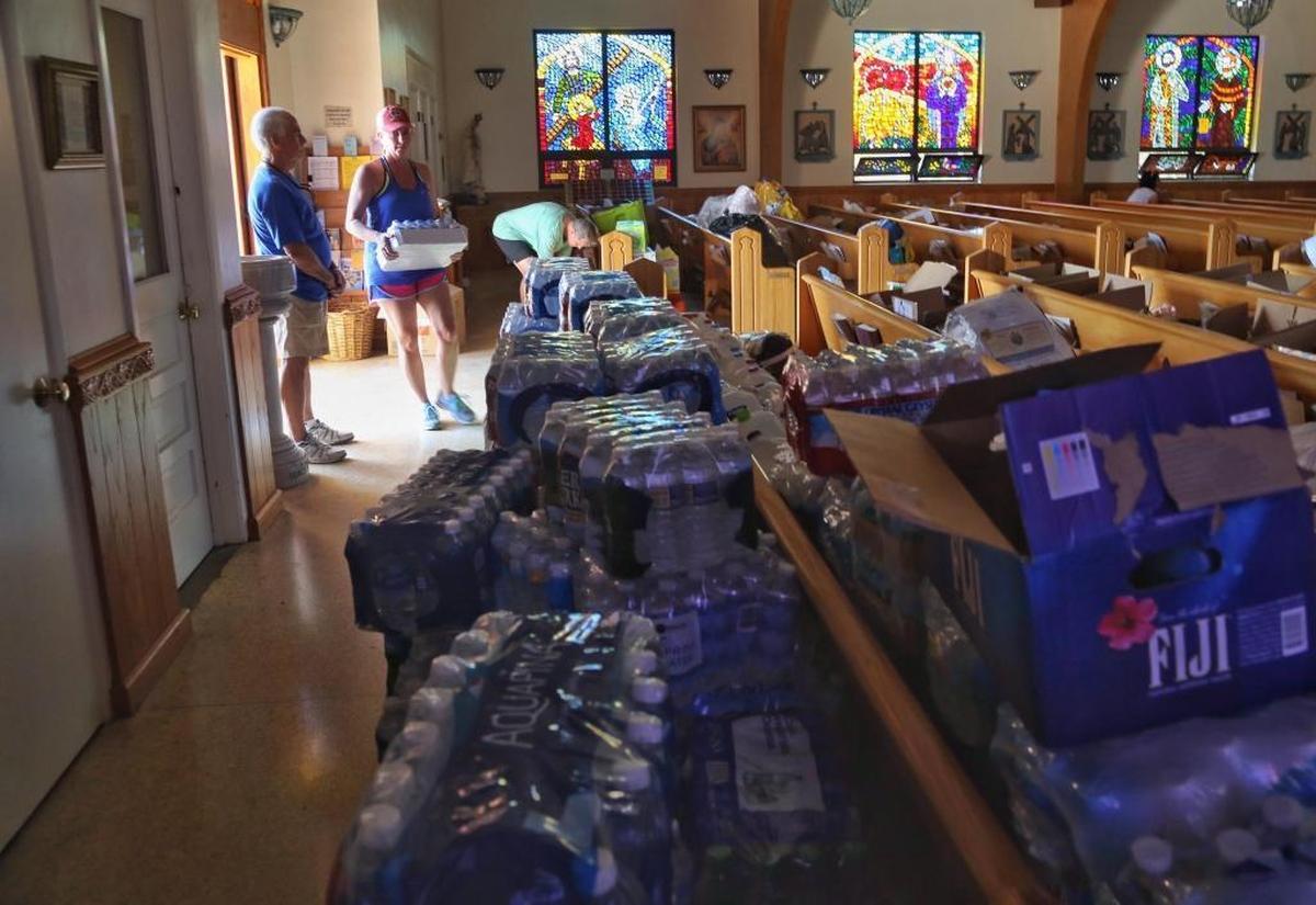 Usher Bruce Ferraro, left, stands near the open door of San Pablo Catholic Church on Marathon Key as Sandy Burton, center, and husband Rich, right, drop off water and other items donated by residents of Palm City.