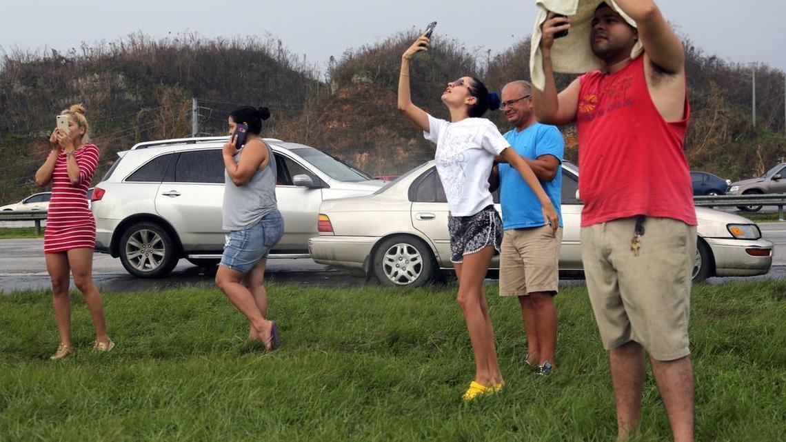Ashley Gonzalez, center, points her cell phone towards a cell tower as she and others try to place calls to the U.S. mainland outside of Dorado on PR22 in Puerto Rico on Saturday.