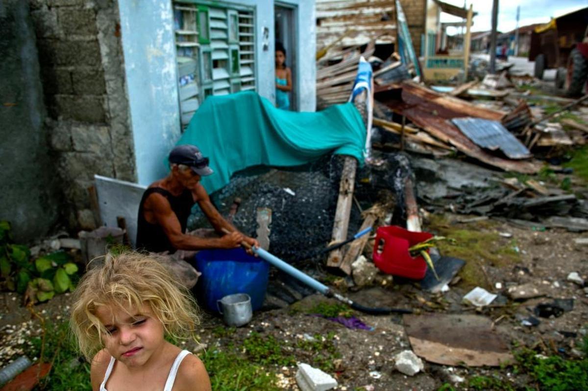 A girl walks beside a man trying to collect water from a pipe next to the remains of a house destroyed by Hurricane Irma in Isabela de Sagua, Cuba on Monday.